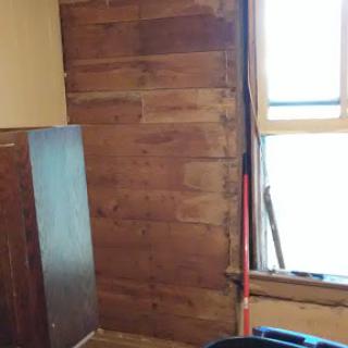A view of a room featuring wooden paneling and a window, indicative of ongoing renovations.