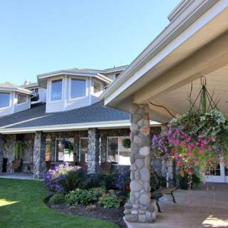 A beautiful house with stone pillars and a landscaped garden featuring hanging flower baskets.