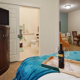A cozy bedroom with a wine bottle and glasses on a tray, featuring an open view of the bathroom and dining area.