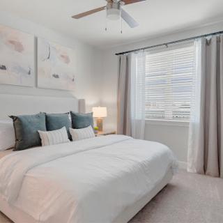 A modern and serene bedroom featuring light colors, stylish bedding, and elegant window treatments.