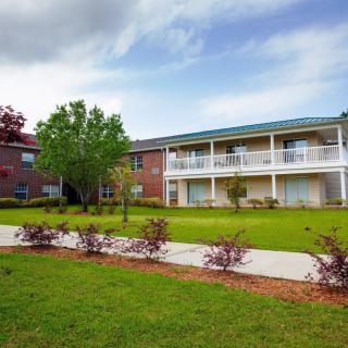 A two-story building with a grassy courtyard and pathway under a partly cloudy sky.