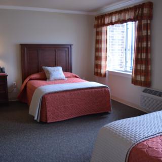 A neatly arranged hotel room featuring two beds with matching bedspreads and a large window with curtains.