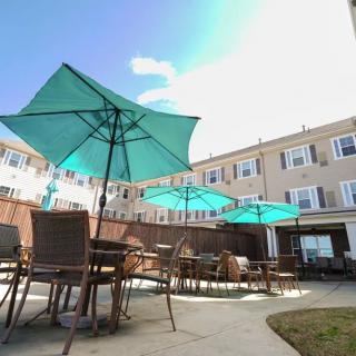 A sunny patio area with tables, chairs, and teal umbrellas, adjacent to a multi-story building.