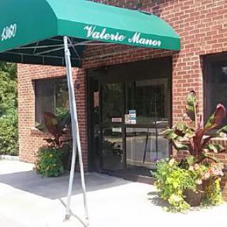 Entrance of a building with a green awning and decorative plants.