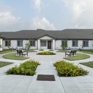 A symmetrical garden with benches and pathways leading to a building under a cloudy sky.