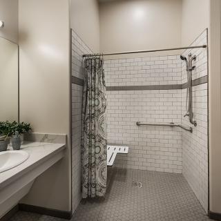 A modern, accessible bathroom featuring a tiled shower area with grab bars and a foldable seat.
