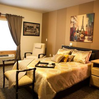 A cozy bedroom with elegant decor, featuring a comfortable bed, chairs, and wall art.