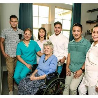 A family gathering with a caregiver and an elderly woman in a wheelchair.