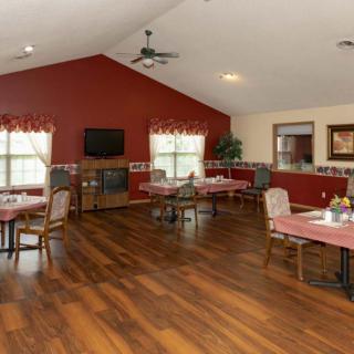 A cozy dining area with several tables and chairs, featuring a red accent wall and hardwood floors.