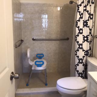 Bathroom with a shower equipped with a safety chair and grab bar.