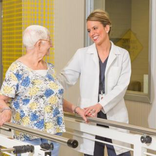 A healthcare professional assists an elderly woman with physical therapy exercises.