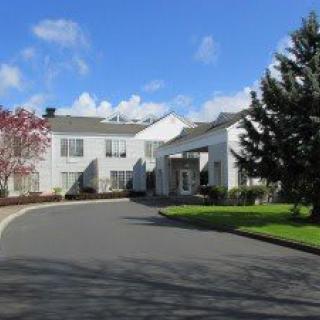 A residential building with a curved driveway and surrounding greenery under a blue sky.