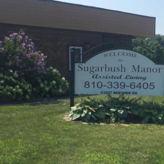 Sign for Sugarbush Manor Assisted Living in front of a building.
