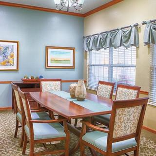 A well-furnished dining room with a wooden table, chairs, decorative artwork, and natural light from the window.