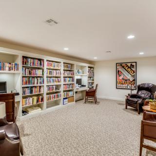 A cozy home library with bookshelves, armchairs, and a computer desk.