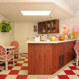 A cozy retro kitchen area featuring a wooden bar, pink chairs, and a vibrant checkered floor.