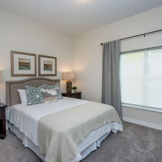 A neatly decorated bedroom featuring a bed with pillows, side tables with lamps, and a large window with curtains.