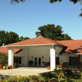 A sunny day view of a residential building with a red roof and surrounding greenery.