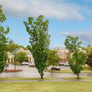 A serene view of a parking lot surrounded by trees and buildings under a partly cloudy sky.