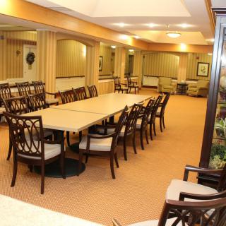 A spacious dining or conference room with long tables and multiple chairs, decorated with neutral tones and well-lit with ceiling lights.