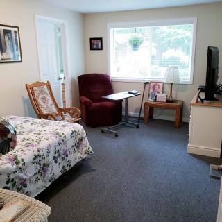 A cozy living room with a bed, armchair, television, and window offering a view.