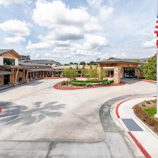A modern building with a circular driveway and landscaped surroundings under a cloudy sky.