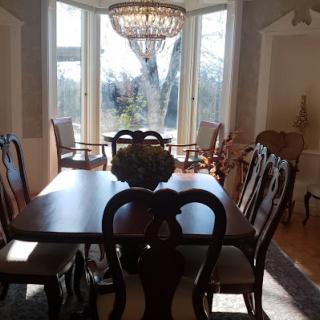 A sunlit dining room with a large table, elegant chairs, and a chandelier.