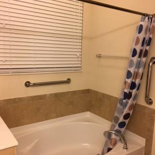 A bathroom featuring a bathtub with a colorful shower curtain, grab bars, and window blinds.