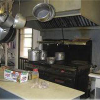 A commercial kitchen with hanging pots, a large stove, and various cooking equipment.