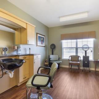 A well-lit hair salon with chairs and a sink, featuring a large window and wooden flooring.