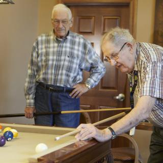 Two elderly men playing pool in a recreational setting.