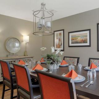 A stylish dining room with orange-accented chairs, a modern chandelier, and elegant table settings.