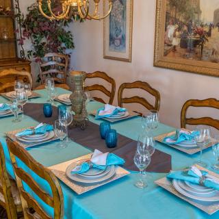 A beautifully set dining table with turquoise accents and elegant dinnerware, surrounded by wooden chairs and illuminated by a chandelier.