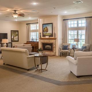 A cozy and well-decorated living room featuring a fireplace, multiple sofas, large windows with curtains, and a ceiling fan.
