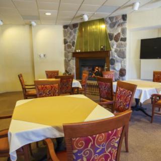 A cozy dining room with neatly arranged tables and a stone fireplace.