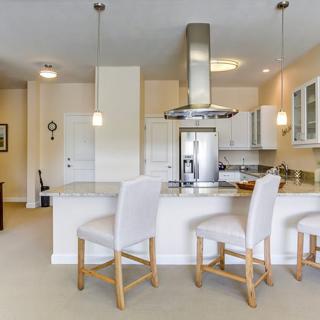 A modern kitchen with white bar stools and stainless steel appliances.