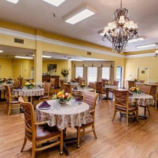 A cozy dining area with round tables, wooden chairs, and a chandelier hanging from the ceiling.