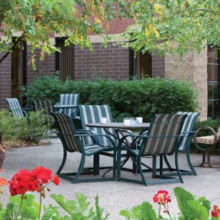 A serene outdoor seating area featuring a table surrounded by chairs, set against a backdrop of lush greenery.