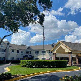 A hotel building surrounded by trees and a clear blue sky with clouds.