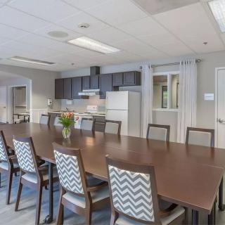 A modern conference room featuring a long table, chairs, and an adjacent kitchen area.