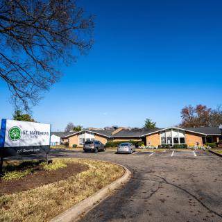 A building with a driveway, cars, and a sign under a clear blue sky.