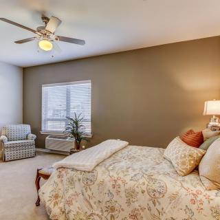 A cozy bedroom with neutral tones, featuring a bed, chair, and a large window.