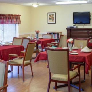 A cozy dining area with tables set for meals, featuring a television and simple decor.