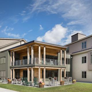 A modern residential building with a wooden porch and balcony, set against a clear blue sky.