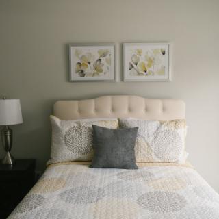 A neatly arranged bedroom with a cushioned headboard, decorative pillows, and framed artwork above the bed.