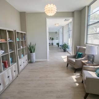 A modern waiting area with comfortable seating, bookshelves, and large windows letting in natural light.