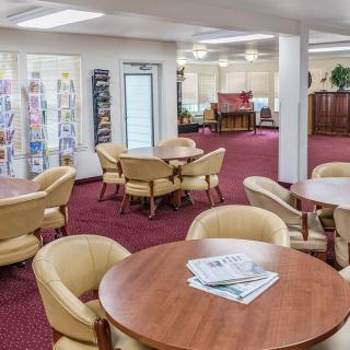 A cozy lobby with seating areas featuring round tables and beige chairs on a red carpet.