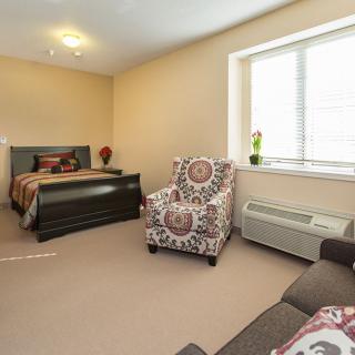 A cozy bedroom with a bed, patterned armchair, and ample natural light from the window.