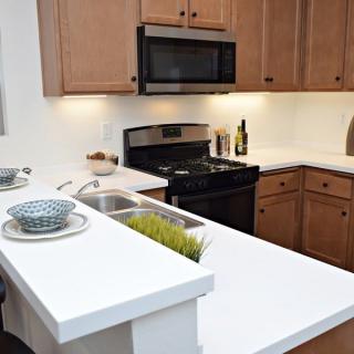 A modern kitchen with wooden cabinets, a microwave above a stove, and a white countertop with bowls.