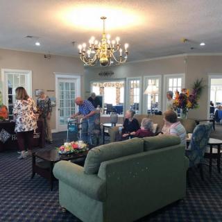 A group of people socializing in a well-lit living room with comfortable furniture and a chandelier.